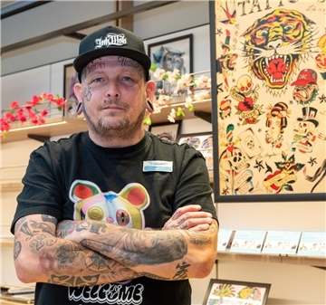 Ein tätowierter Mann blickt in die Kamera.