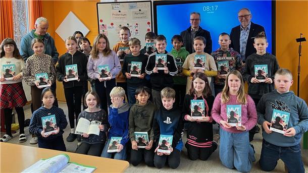 Stolz präsentieren die Kinder ihre nagelneuen Bücher, die die Mitglieder des Rotary-Clubs Bremervörde-Zeven im Gepäck hatten. Im Hintergrund sind Schulleiter Ralf Pochciol (hinten links) und Stefan Tomczak sowie Präsident Arne Suter zu sehen.