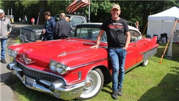Ein Mann in Jeans und T-Shirt lehnt an seinem roten US-Oldtimer der Marke Cadillac