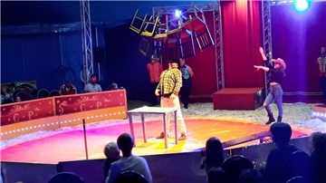 In der Mitte einer Zirkusmanege balanciert ein Akrobat fünf Stühle auf seinem Kinn