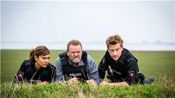 Süher Özlügül (Sophie Dal, l.), Kriminalhauptkommissar Brockhorst (Felix Vörtler, M.) und Henk Cassens (Maxim Mehmet, r.) beobachten eine Situation vom Deich aus.