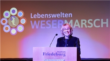 Eine Frau steht auf einer Bühne an einem Podest. 