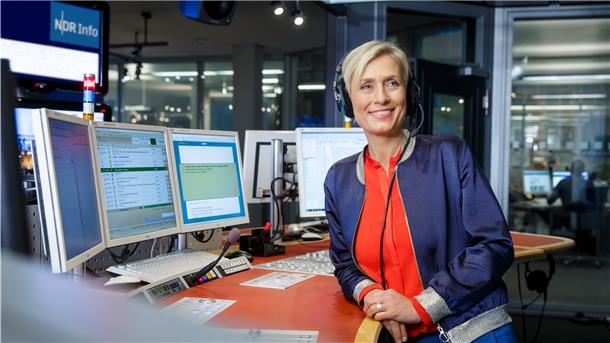 Frau mit Kopfhörer, vor Bildschirmen.