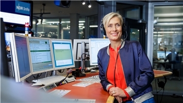 Frau mit Kopfhörer, vor Bildschirmen.