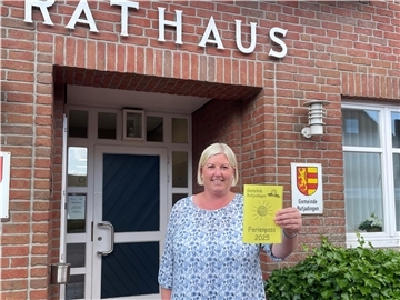 Eine Frau steht vor dem Rathaus und hält ein Ferienpass-Heft in die Kamera.