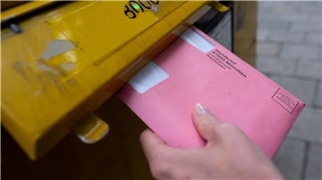 Jemand steckt einen Umschlag mit Briefwahlunterlagen in einen Briefkasten.