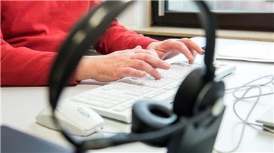 Ein Headset. Im Hintergrund Hände an einer Tastatur.
