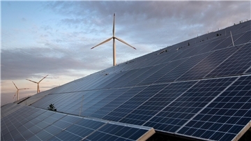 Im Vordergrund sind Photovoltaikanlagen zu sehen, im Hintergrund Windenergieanlagen.