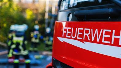 Ein Feuerwehrauto, im Hintergrund Feuerwehrleute