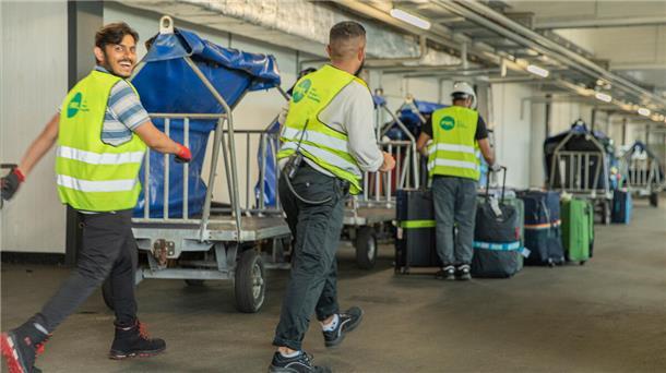 Männer laufen lachend zu den sogenannten "Hamburgern ", Gepäckwagen werden mit den Gepäckstücken beladen.