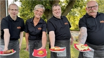 Drei Männer und eine Frau halten belegte Brötchen in die Kamera.