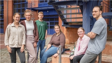 4 Frauen und 2 Männer sitzen und stehen unter einer Treppe.