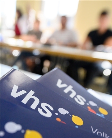 Teilnehmer eines Sprachkurses sitzen hinter dem aktuellen Programm der Volkshochschule. 