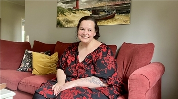 Eine lächelnde übergewichtige Frau sitzt auf einem roten Sofa. 