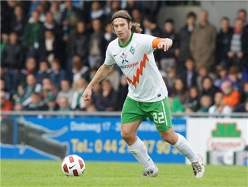 Fußballspieler mit langen Haaren und grün-weißem Trikot im Spiel in einem voll besetzten Stadion