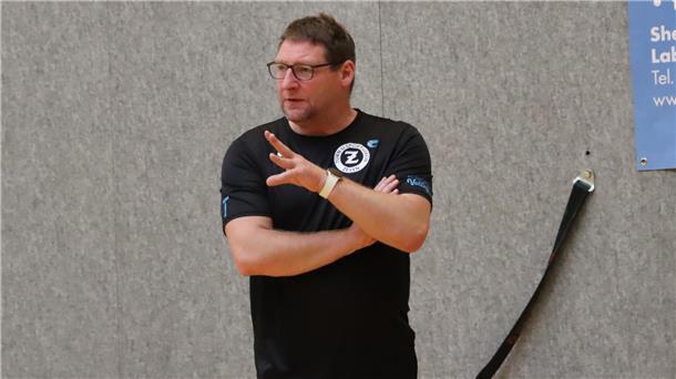 Ein Mann schaut mit verschränkten Armen gespannt einem Volleyballspiel zu. 