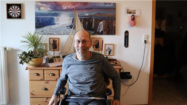 Ein Leben mit MS: Der Kampf eines Zeveners für mehr Selbstständigkeit im Alltag Mann mit Brille im Rollstuhl vor Wohnzimmer-Wand