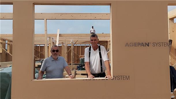 Zwei Männer schauen durch die Fensteröffnung einer Wand in Holzrahmenbauweise
