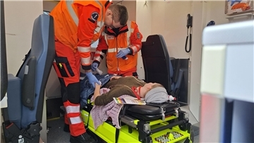 Zwei Rettungssanitäter helfen im Rahmen eines Übungsszenarios einer Person, die im Rettungswagen auf einer Bahre liegt. 
