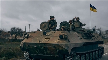 Ukrainische Soldaten zeigen ein Peace-Zeichen während sie mit einem erbeuteten russischen Schützenpanzer fahren.