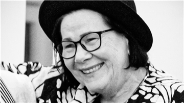 eine Frau mit Brille und Hut lächelt
