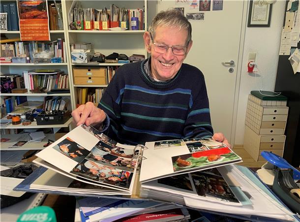 Ein Mann mit Brille und dunkelblauem Pullover blättert in einem Fotoalbum.