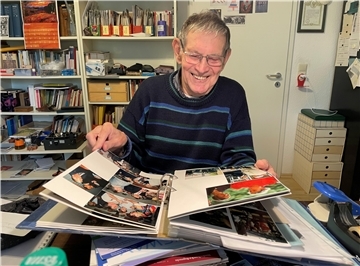 Ein Mann mit Brille und dunkelblauem Pullover blättert in einem Fotoalbum.