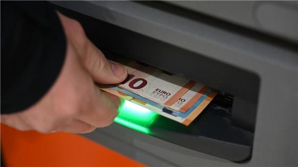 Ein Mann zieht Geldscheine aus dem Ausgabefach eines Geldautomaten
