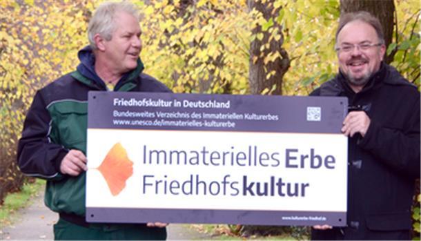 Ein Schild wird am Friedhofszaun angebracht.
