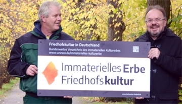 Ein Schild wird am Friedhofszaun angebracht.