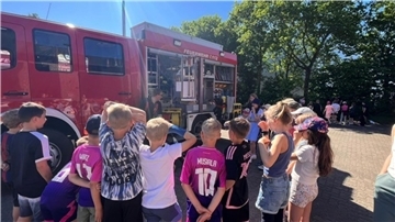 Eine Gruppe Kinder steht im Halbkreis um ein geöffnetes Einsatzfahrzeug der Feuerwehr
