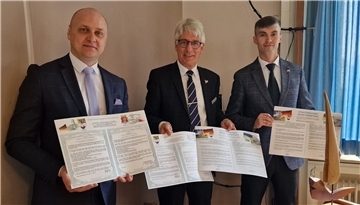 Das Bild zeigt drei Männer, die unterzeichnete Städtepartnerschaftsverträge in die Kamera halten.