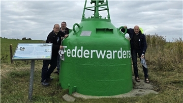 Drei Männer stehen neben der grünen Fahrwassertonne an der Hafeneinfahrt in Fedderwardersiel.