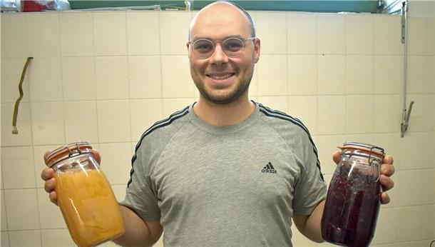 Ein Mann mit einer Glatze hält zwei Einmachgläser in den Händen.