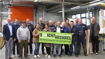 Mehrere Menschen stehen nebeneinander und präsentieren für den Fotografen ein Plakat, auf dem "Schichtwechsel" steht. 