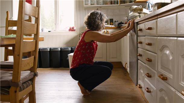 Die besten Pflegetipps für die Spülmaschine: So bleibt Ihr praktischer Helfer in der Küche immer fit Eine Frau in einem roten Shirt hockt in ihrer Küche vor der Spülmaschine.
