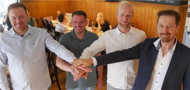 Vier Männer stehen nebeneinander und legen je eine Hand auf die Hände der anderen.