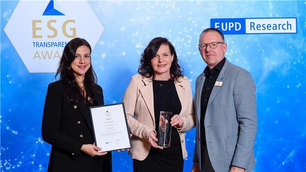 Zwei Frauen und ein Mann mit Urkunde und einem Award.