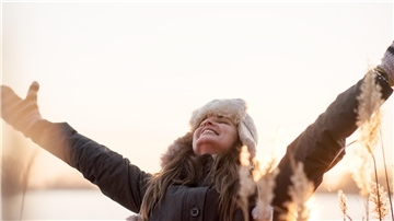 Eine Frau in Winterkleidung und mit Mütze genießt die Sonne.