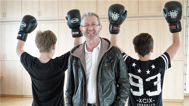 Ein Mann steht zwischen zwei Jugendlichen, die Boxhandschuhe tragen.