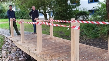 Zwei Männer stehen an einer Holzbrücke.