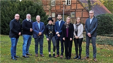Gruppe von Menschen in Garten vor Fachwerkhaus; in der Mitte eine Schornsteinfegerin
