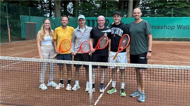 Mehrere Personen stehen auf einem Tennisplatz und halten Tennisschläger in den Händen.