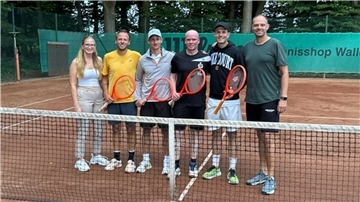 Mehrere Personen stehen auf einem Tennisplatz und halten Tennisschläger in den Händen.