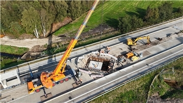 Ein großes Betonteil wird über einer Autobahn von einem Kran angehoben.