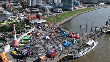 **ALT-Text:**
Luftaufnahme vom Willy-Brandt-Platz in Bremerhaven während eines Großevents mit bunten Pavillons, Aktionsflächen und Menschenmengen am Weserufer.