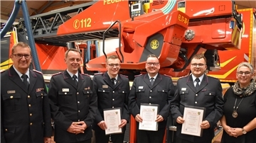 Fünf Männer und eine Frau stehen vor einem Feuerwehrauto.