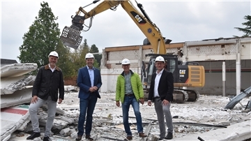 Vier Männer mit Bauhelmen stehen in einer Baustelle vor einem Kran.