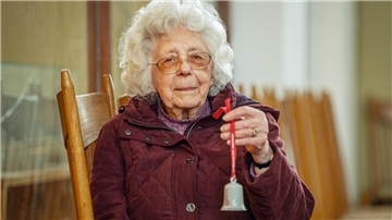 Eine Seniorin hält ein Glöckchen in der Hand.