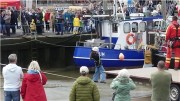 Viele Menschen in einem Hafen beobachten ein Mädchen auf einer Slackline über dem Hafenbecken.